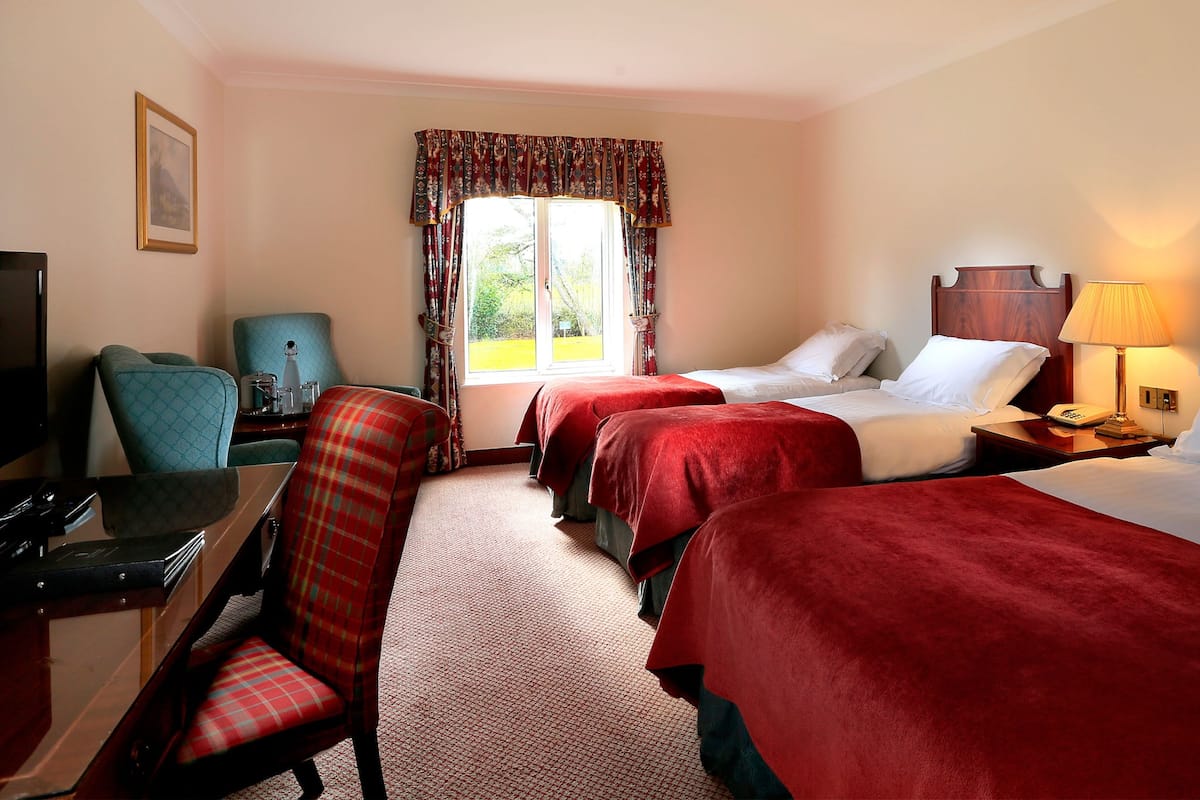 A hotel room with two beds, a desk with a chair, a television, and a window with curtains.