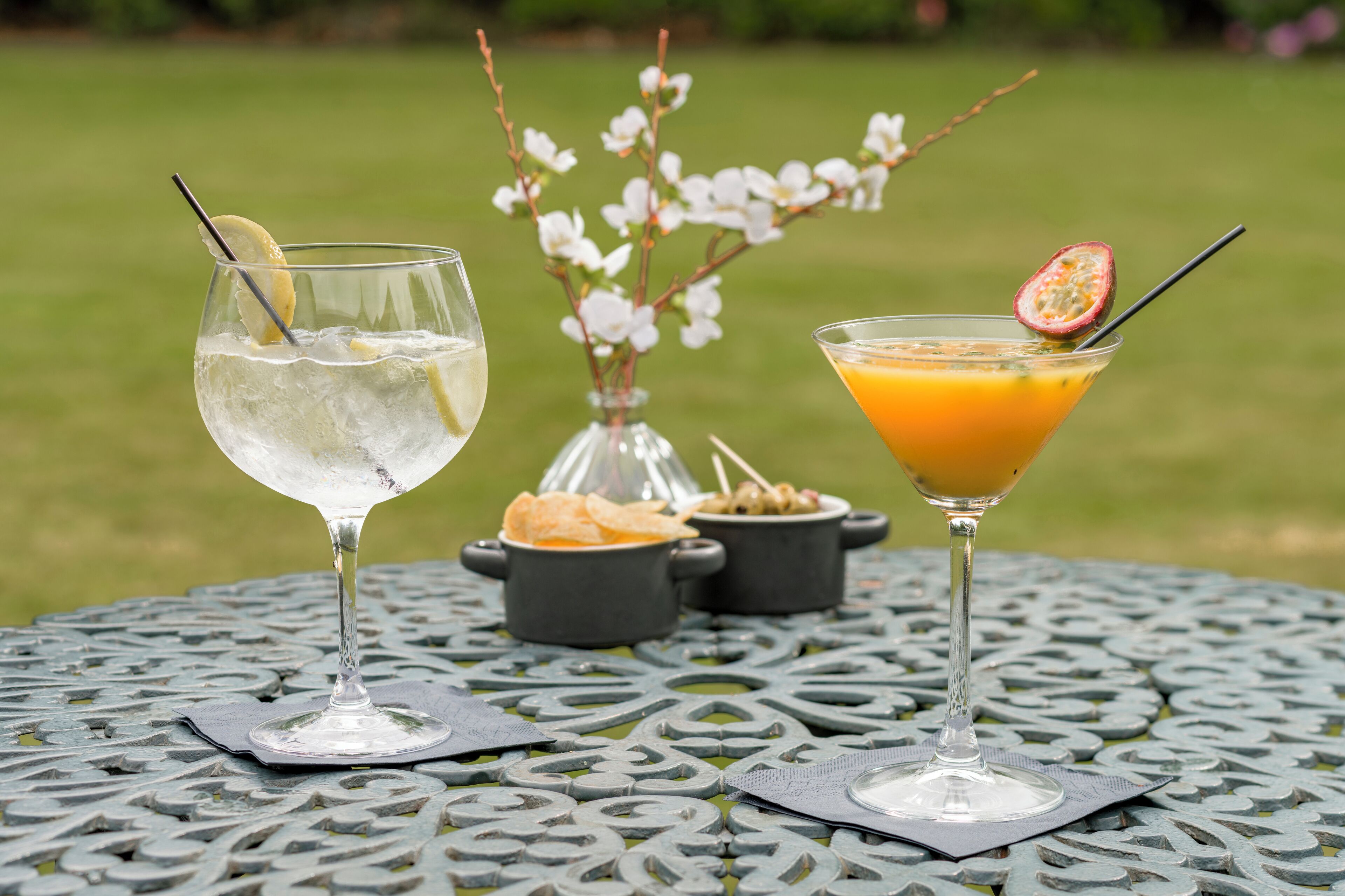 Twee drankjes op een metalen tafel, met een bloemstuk op de achtergrond.