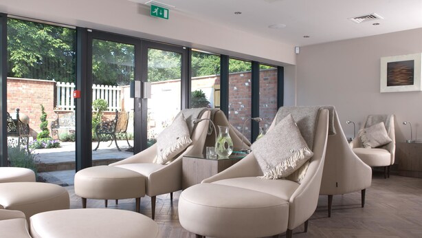 A modern lounge area with leather chairs and ottomans, large windows, and a view of the outdoors. -  Macdonald Craxton Wood Hotel & Spa, Chester (Ellesmere Port)