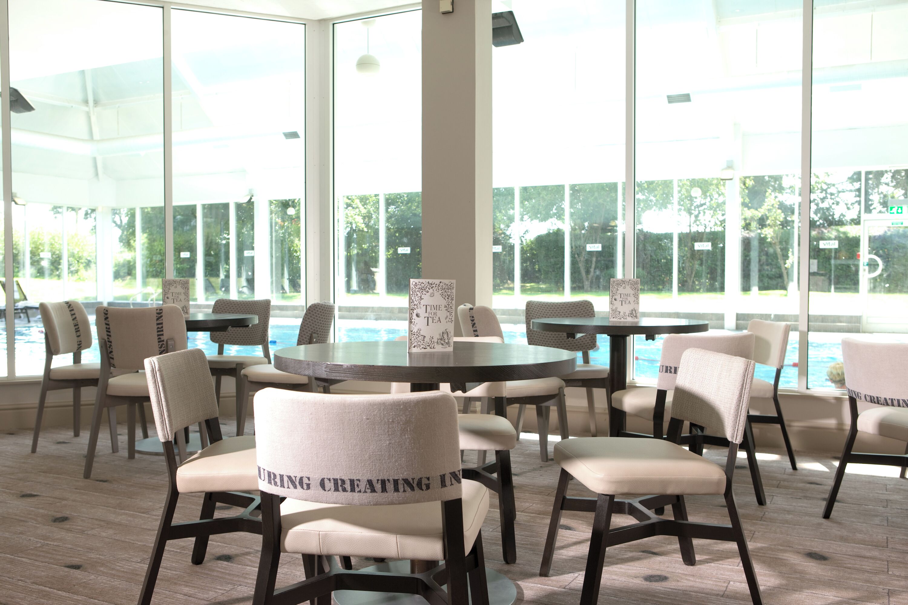 A bright indoor area with large windows, multiple tables, and chairs arranged for dining.