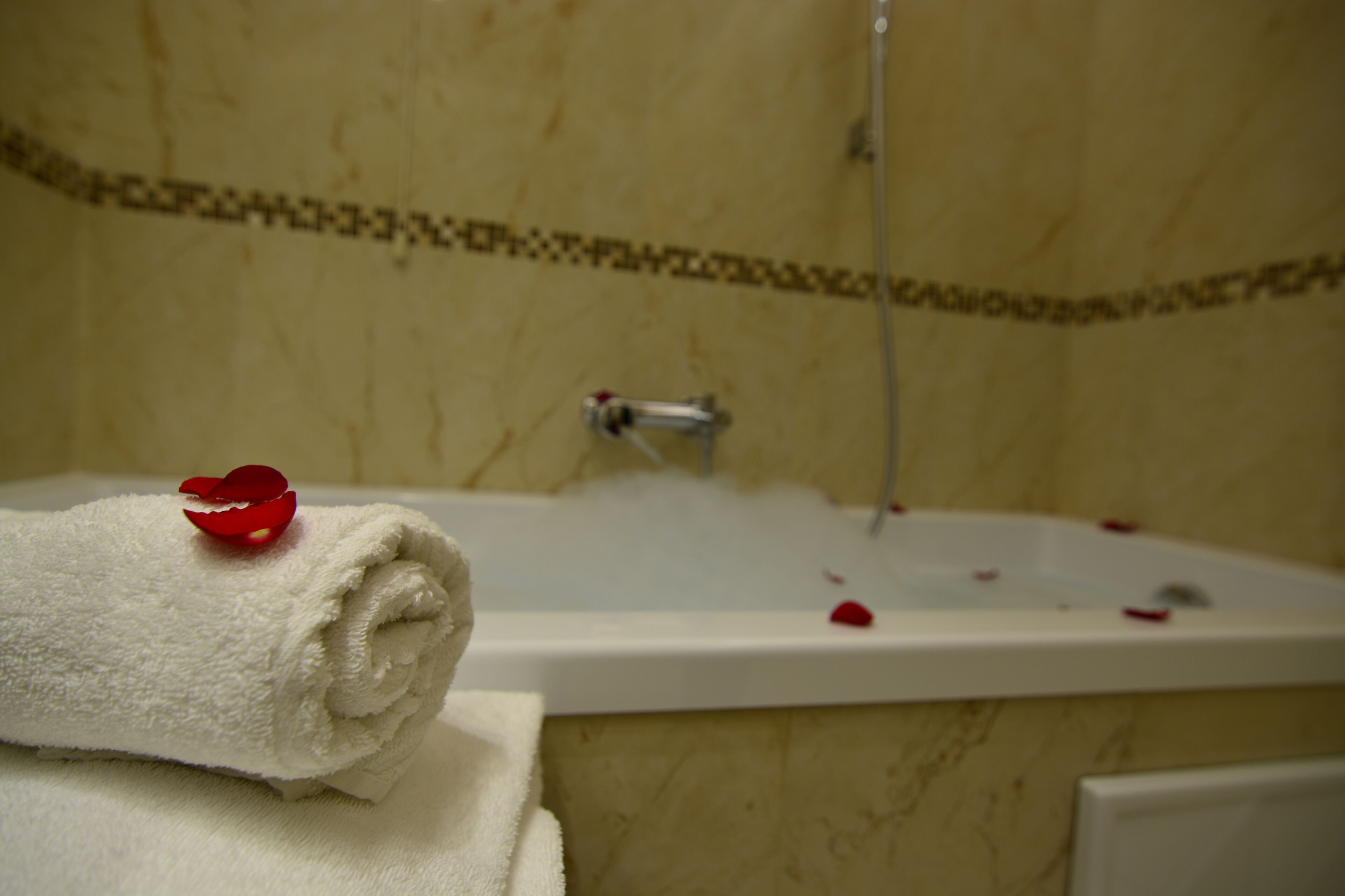 A bathroom with a bathtub, a towel, and a red rose petal on the edge.