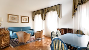 A room with a blue sofa, wicker chairs, a dining table, and curtains with gold trim. - San Marco Palace (Venice)