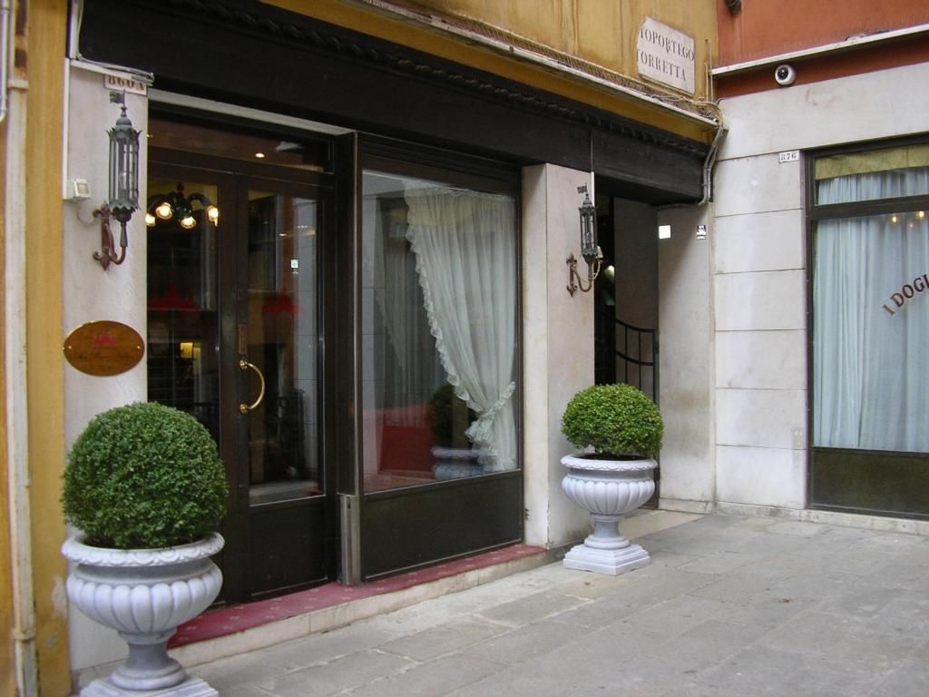 Entrada de hotel con una puerta negra, un letrero sobre la puerta y dos macetas con plantas en la acera.