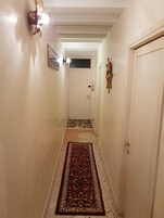 Un pasillo estrecho con un tapete estampado, una puerta al final y lámparas fijadas a la pared.