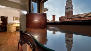 A room with a glass table reflecting a building and a clock tower, a leather bag on the table, and a sofa in the background. - San Marco Palace (Venice)
