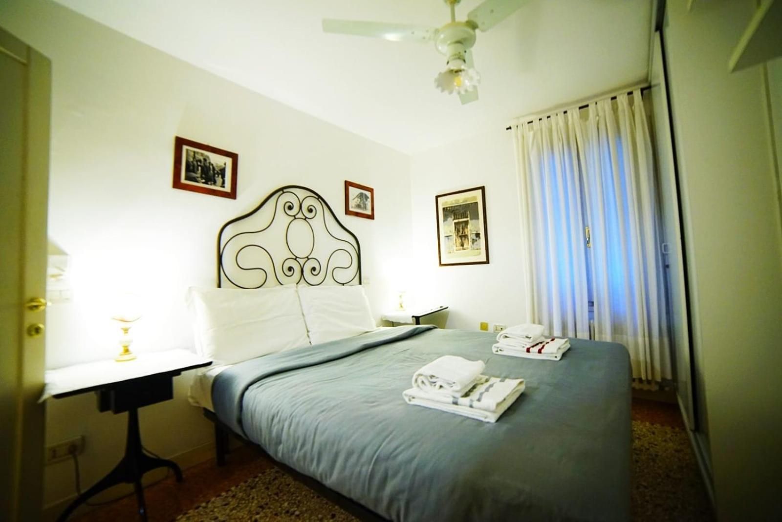 Una habitación de hotel con cama, escritorio, silla, ventilador de techo y cortinas.