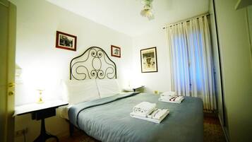Una habitación de hotel con cama, escritorio, silla, ventilador de techo y cortinas.