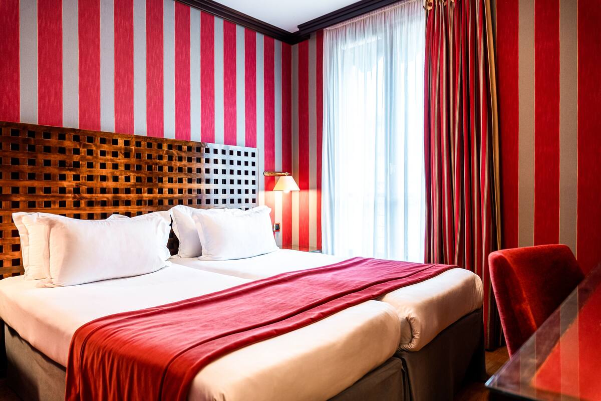 A hotel room with a large bed, a wooden headboard, a red and white striped wall, and a red chair.