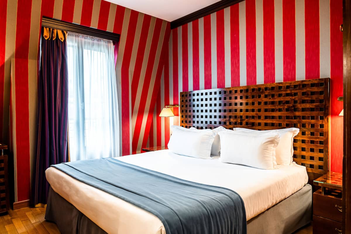 A hotel room with a bed, curtains, a headboard, and a nightstand.