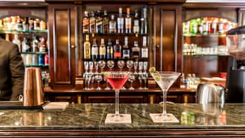 A bar area with two martini glasses on coasters, a copper mug, and a barista preparing drinks.
