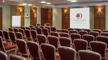 A conference room with rows of red chairs, a projection screen, and wooden paneling.