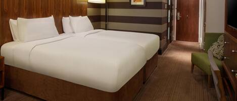 A hotel room with a large bed, a bedside lamp, a framed picture on the wall, and a green chair.