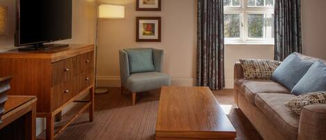 A living room with a TV, wooden furniture, a sofa, a chair, and a window with curtains.