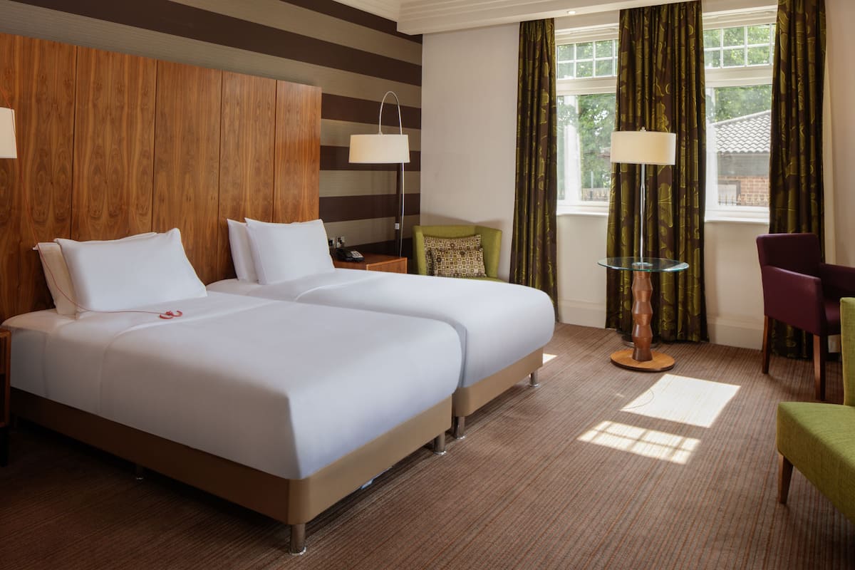 A hotel room with two beds, a desk, a chair, and a table with lamps.