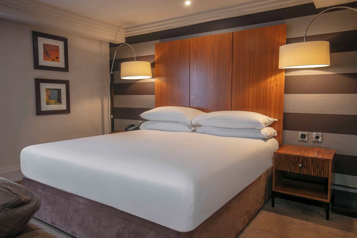 A hotel room with a large bed, two bedside lamps, a wooden nightstand, and two framed pictures on the wall.