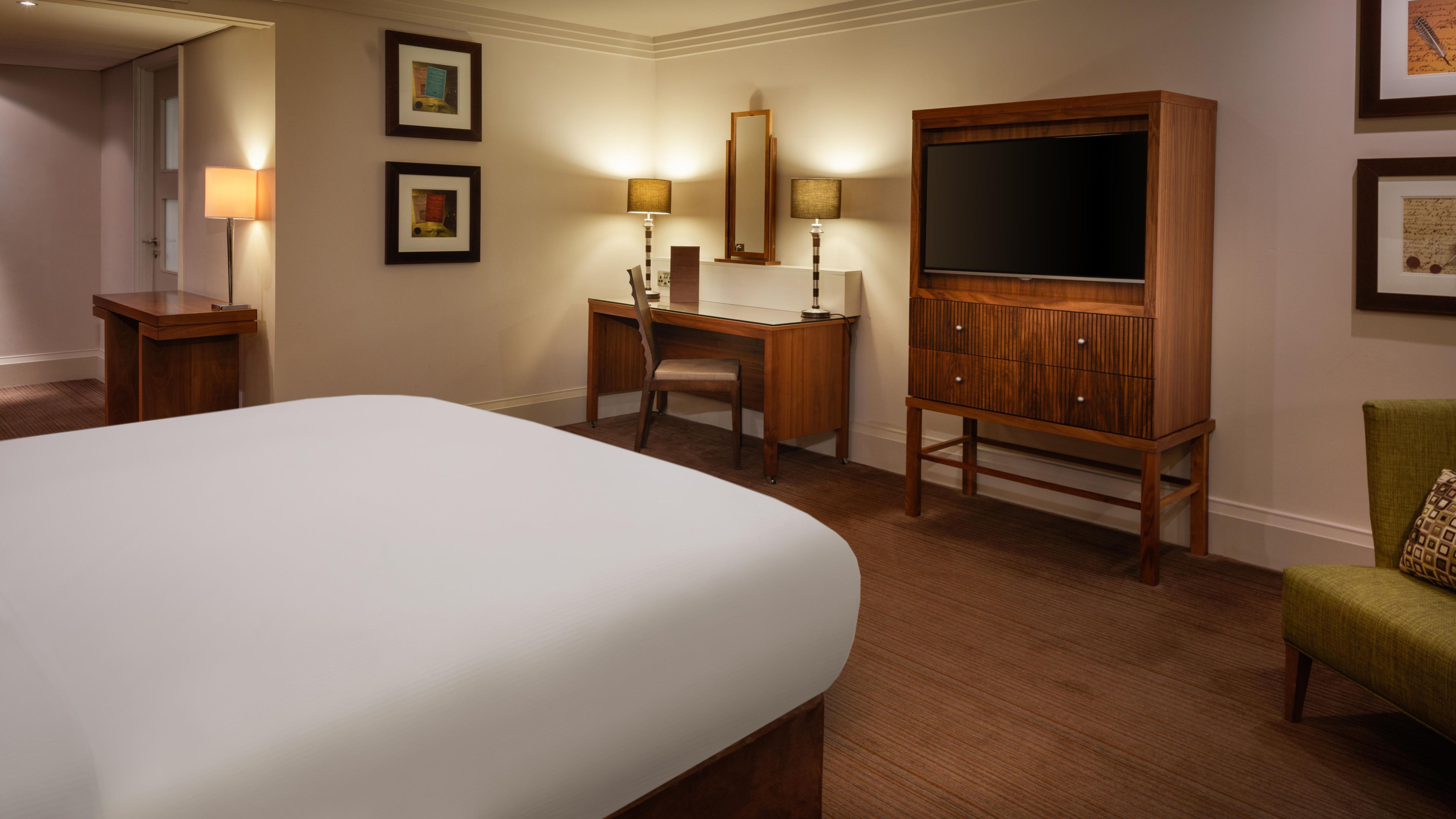 Une chambre d’hôtel avec un grand lit, un bureau avec une chaise, une télévision et des tableaux encadrés au mur.