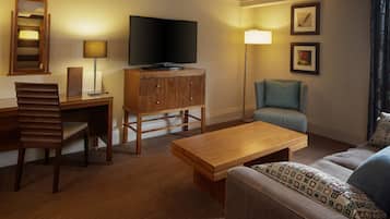 A hotel room with a wooden desk, a television, a sofa, and a lamp.