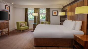 Ein Hotelzimmer mit einem großen Bett, einem Fernseher, einem grünen Sessel, einem kleinen Tisch und zwei Lampen.