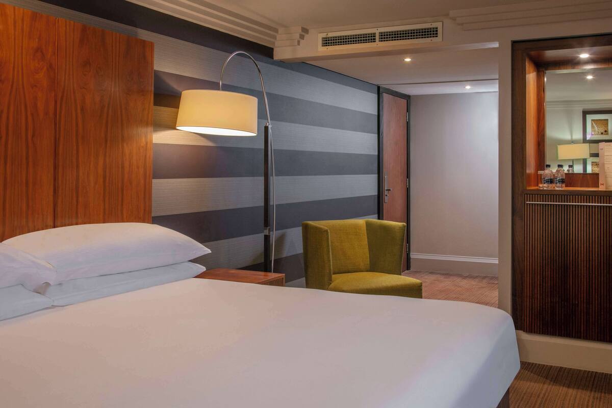 A hotel room with a bed, a nightstand, a lamp, a chair, and a mirror.