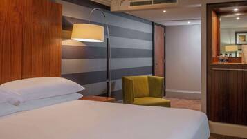 A hotel room with a bed, a nightstand, a lamp, a chair, and a mirror.