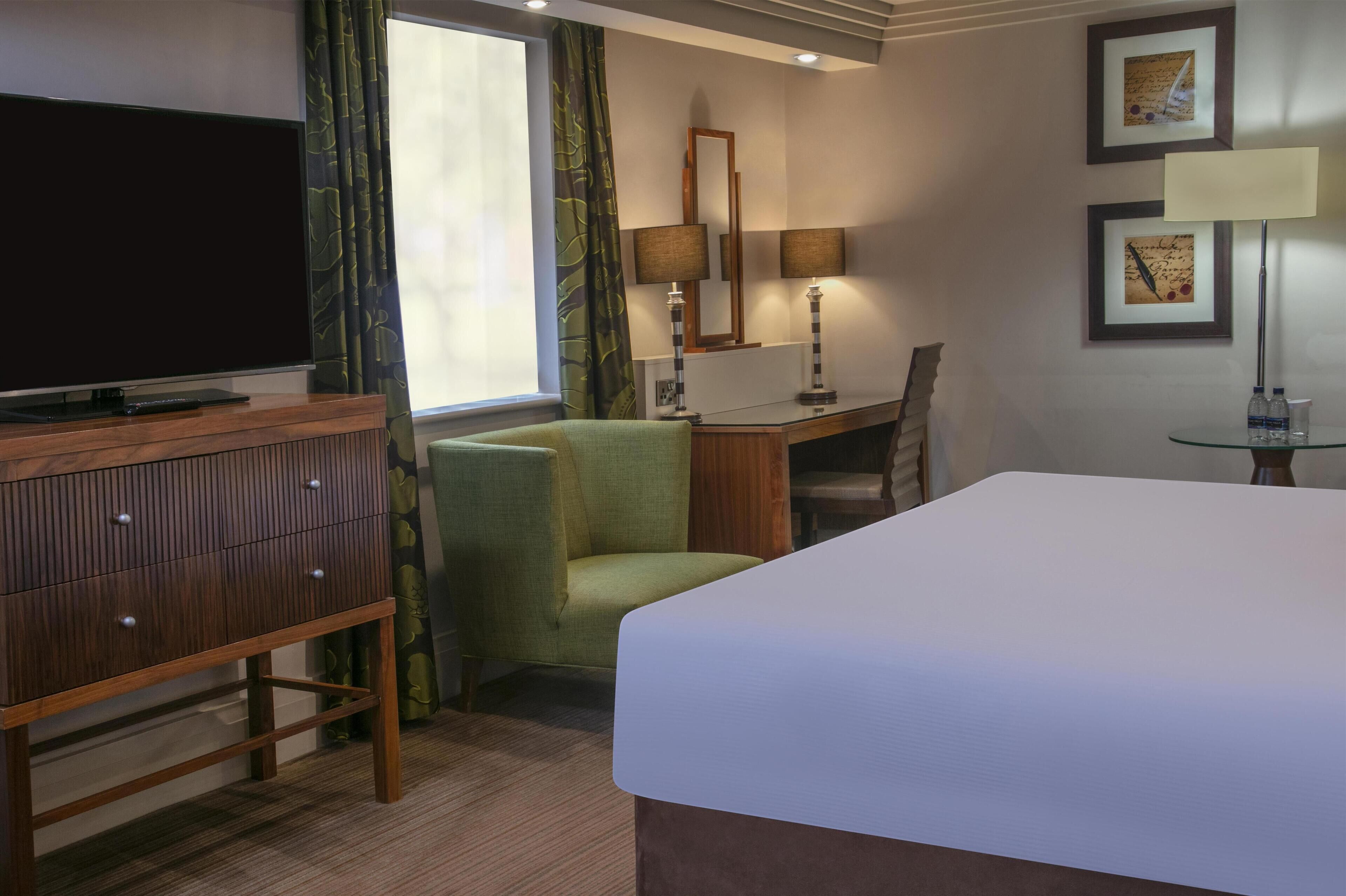 A hotel room with a bed, a desk, a chair, a television, and a lamp.