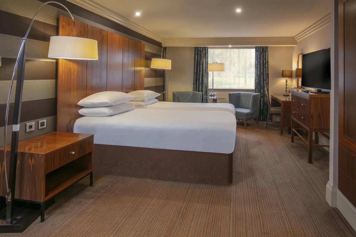 A hotel room with a large bed, a desk, a chair, a TV, and a lamp.