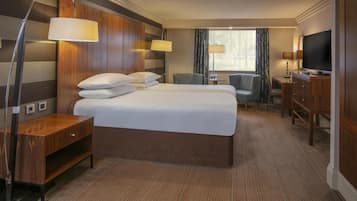 Habitación de hotel con una cama grande, un escritorio, una silla, un televisor y una lámpara.