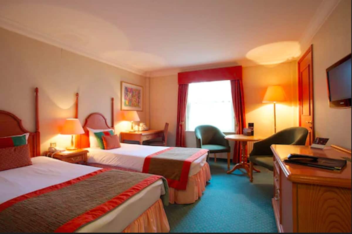 A hotel room with two beds, a desk, a chair, a TV, and a window with curtains.