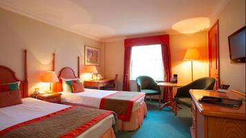 Quarto de hotel com duas camas, uma escrivaninha, uma cadeira, uma televisão e uma janela com cortinas.