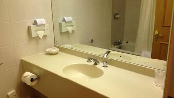 A bathroom with a sink, mirror, toilet, and a shower area.