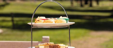 A three-tiered dessert stand with various pastries and sandwiches on a wooden table outdoors.