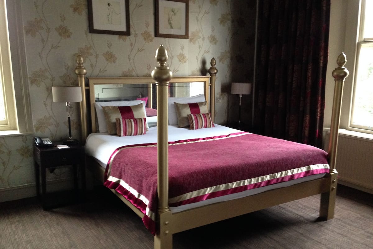 A four-poster bed with a red and white bedspread, a bedside table with a lamp, and a telephone on the nightstand.