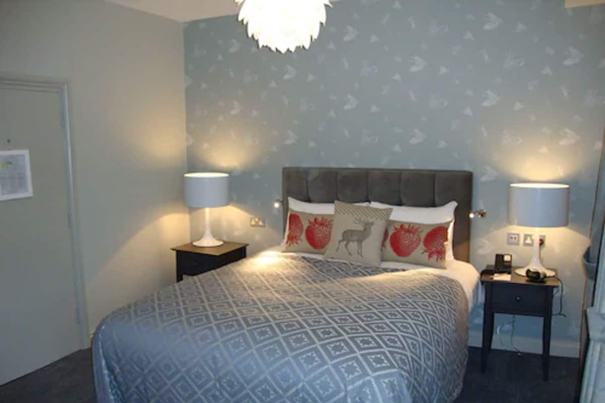 A neatly arranged bedroom with a patterned bedspread, two bedside tables with lamps, and a headboard with decorative pillows.