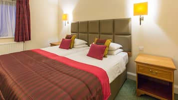 A double bed with a red and brown checkered bedspread, two bedside tables with lamps, and a wooden nightstand with drawers.