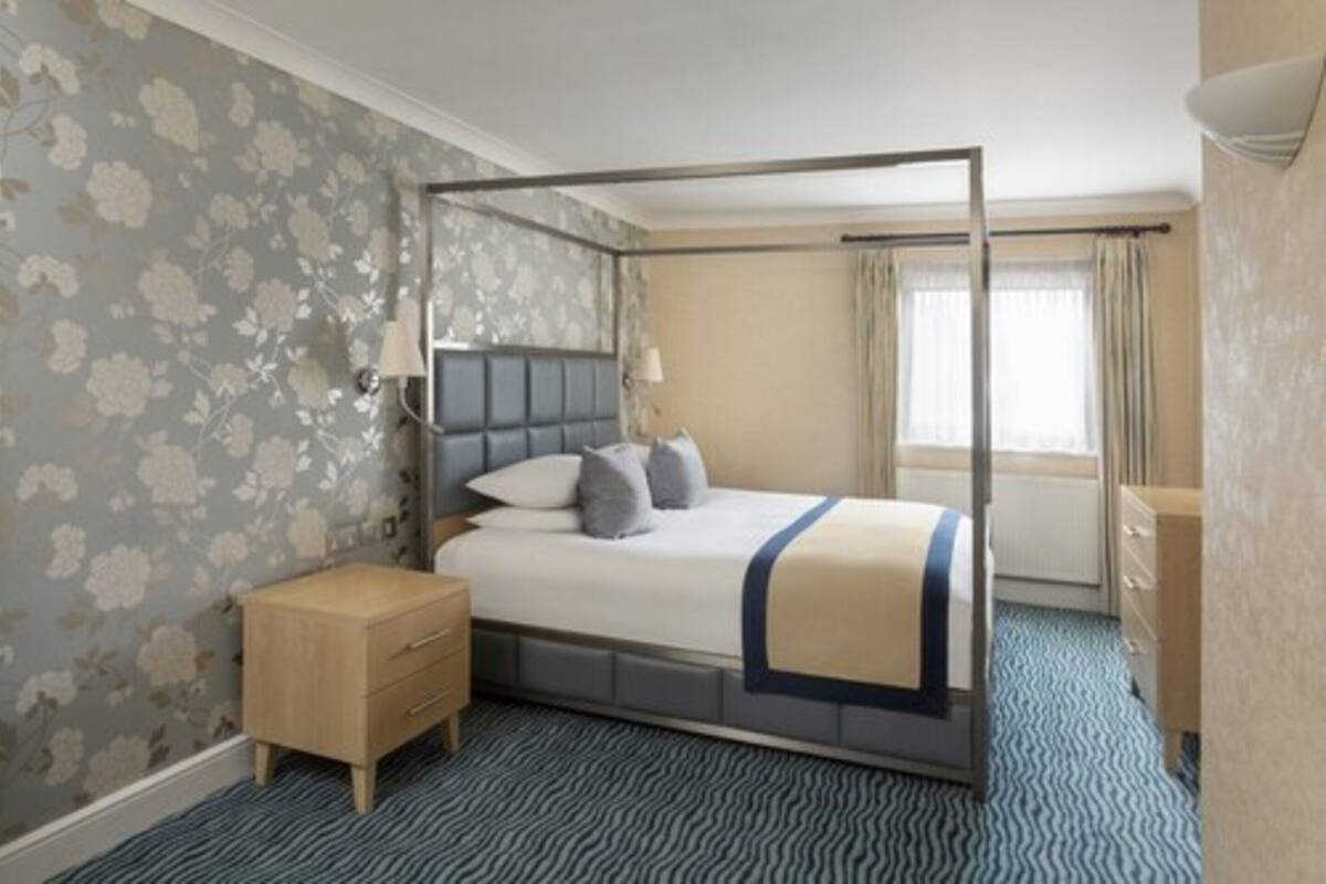 A hotel room with a four-poster bed, a bedside table, a nightstand, and a dresser.