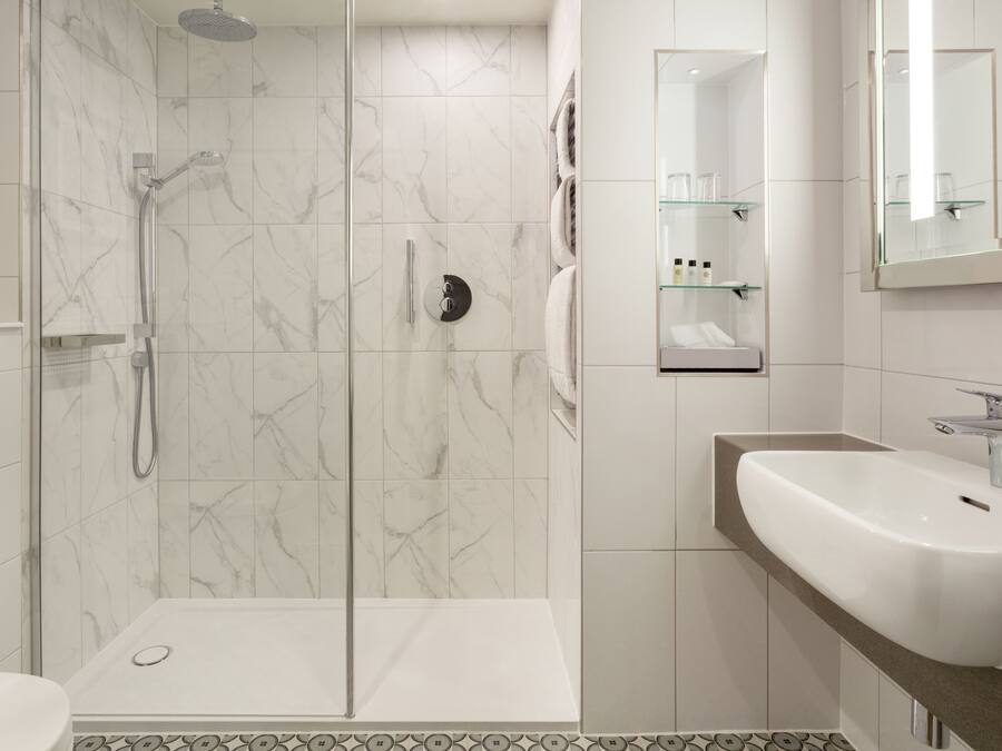 Une salle de bain moderne avec une douche à parois de verre, un lavabo blanc et un miroir au-dessus du lavabo.