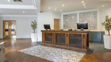 A reception area with a wooden desk, two computer monitors, and a large floral artwork on the wall.