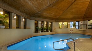 Una piscina interior con paredes de azulejos, techo de madera y plantas en macetas.