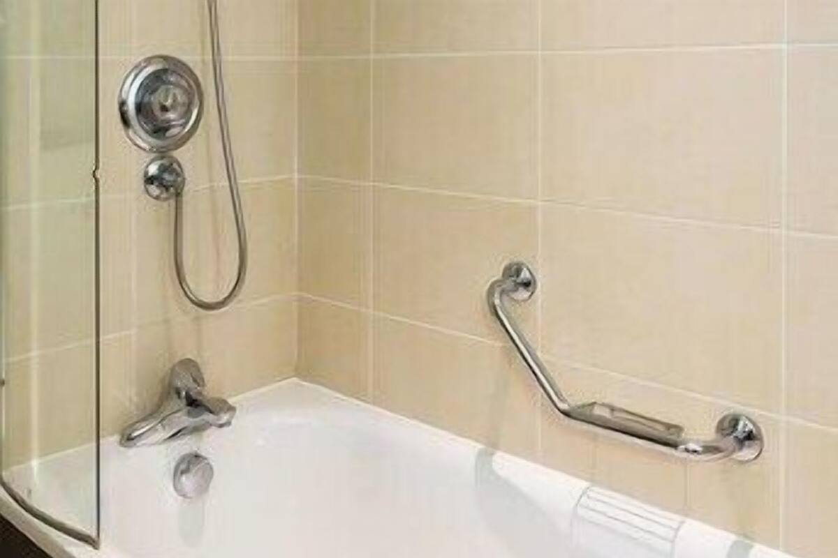 A white bathtub with a handheld showerhead, a grab bar, and a towel on the edge.