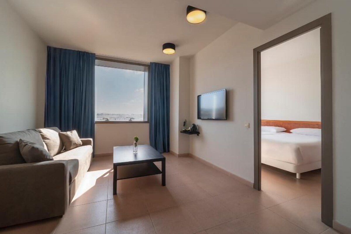 A hotel room with a sofa, a small table, a TV, and a bed.