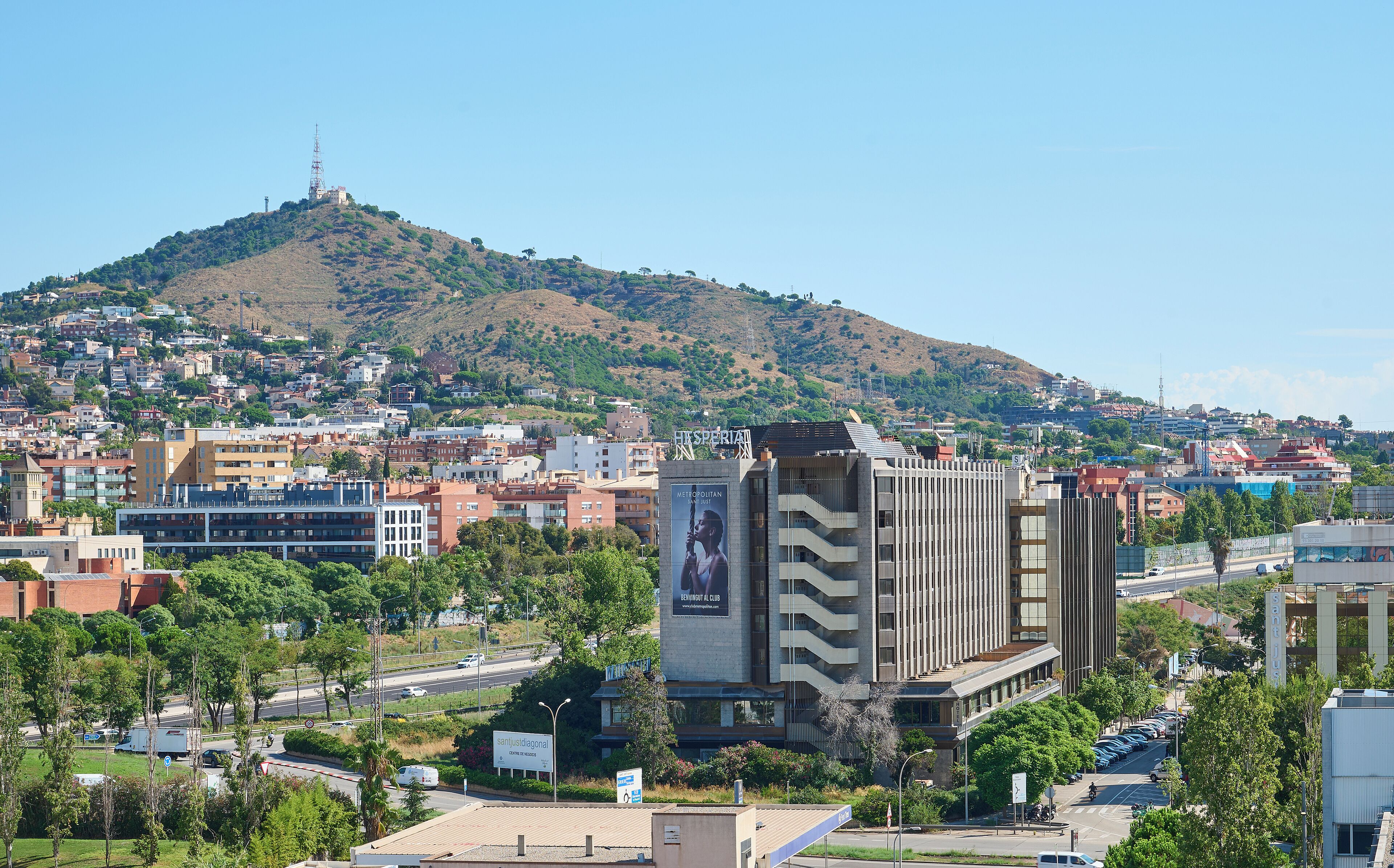 Une vue urbaine mettant en évidence un bâtiment imposant, sur lequel on peut voir un grand panneau publicitaire et une enseigne indiquant « Sanjustiagonal Centre de Recursos ».