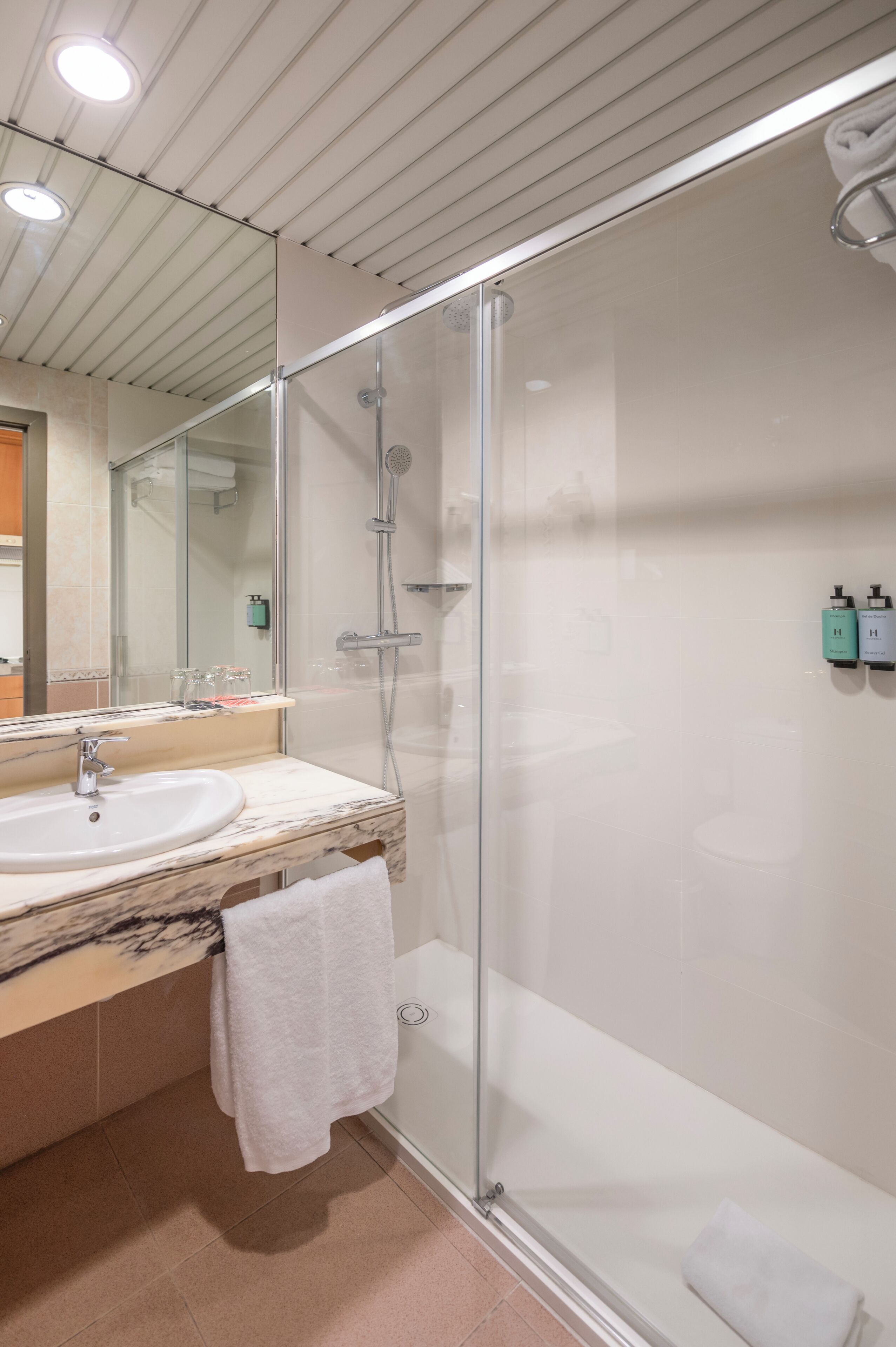 Un baño moderno con ducha de vidrio, un lavabo con encimera de mármol y un espejo sobre el lavabo.