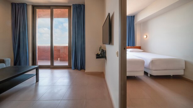 A hotel room with a bed, a desk, a TV, and a sliding glass door to the outside. - Apartamentos Hesperia Sant Joan (Sant Joan Despi)
