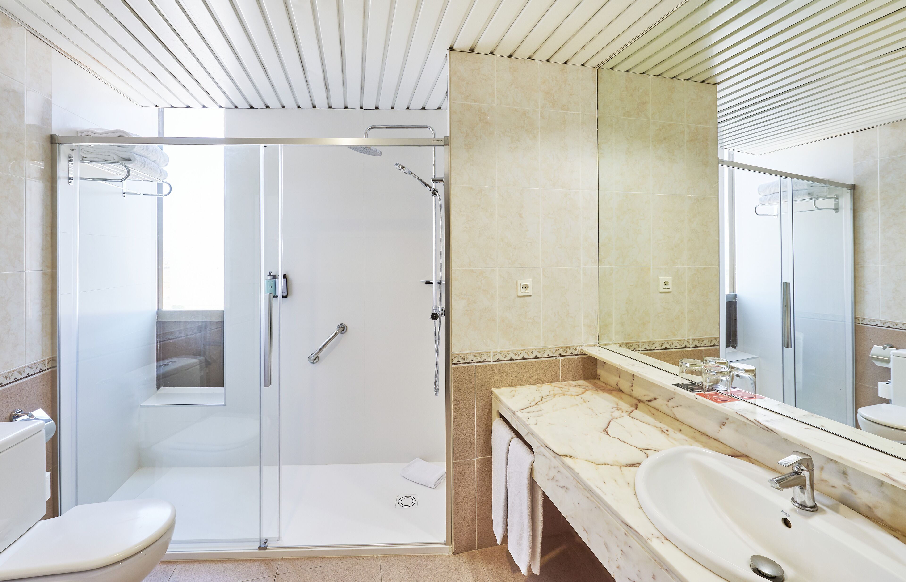 Un baño moderno con cabina de ducha acristalada, tocador de mármol y un espejo grande.