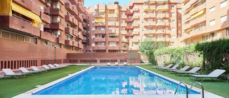 Una piscina rodeada de césped y sillones de descanso.