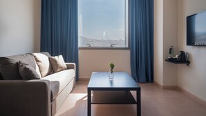 A modern hotel room with a sofa, a small table with a vase, a TV mounted on the wall, and a window with curtains. - Apartamentos Hesperia Sant Joan (Sant Joan Despi)