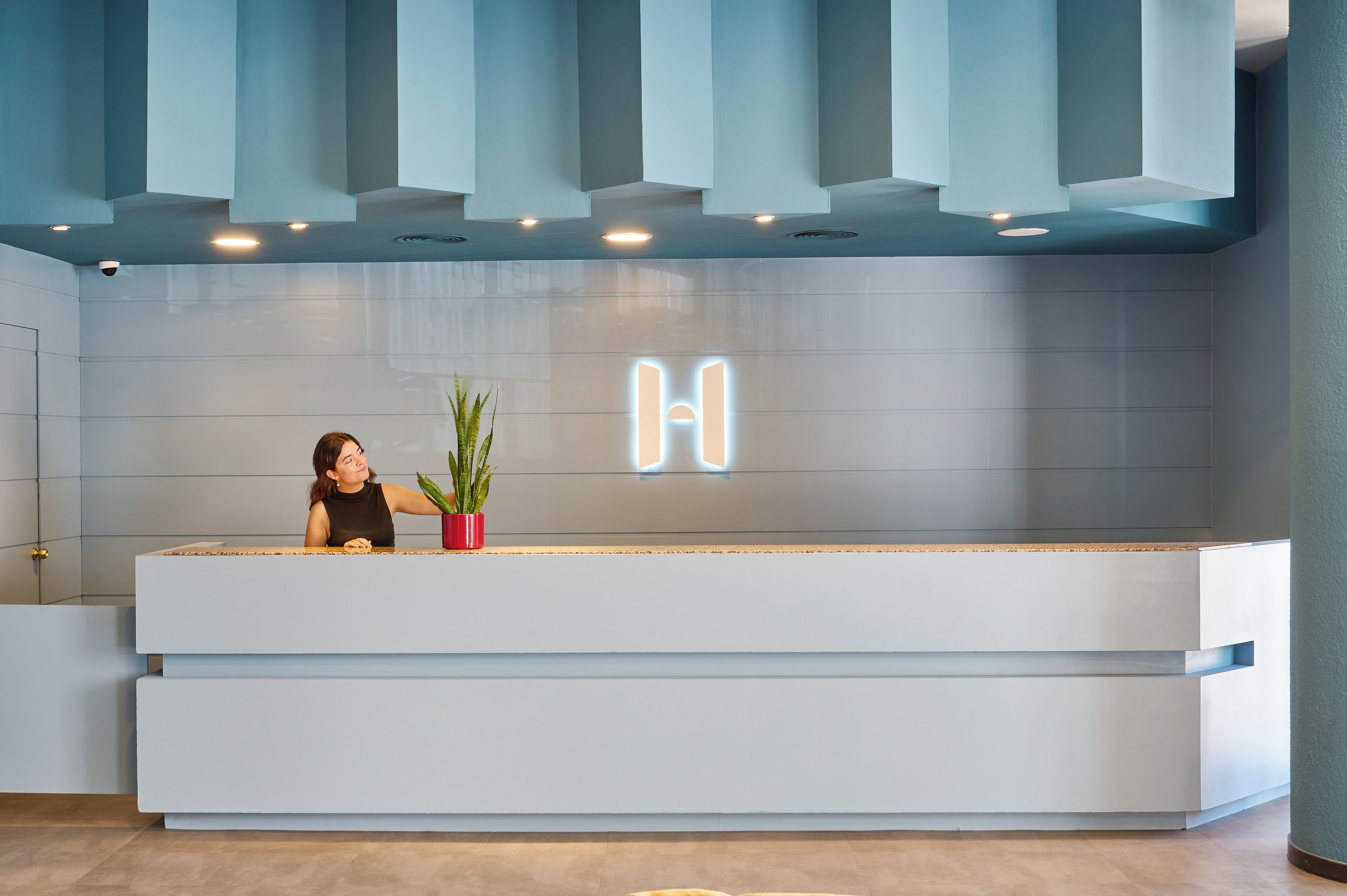 A reception desk with a modern design, featuring a light blue color scheme and a prominent illuminated 'H' sign.