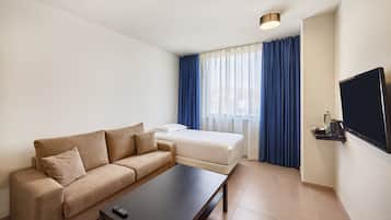 Habitació d'hotel moderna amb un sofà, una taula petita, un televisor i una finestra amb cortines.