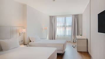 A hotel room with two beds, a desk, and a TV.