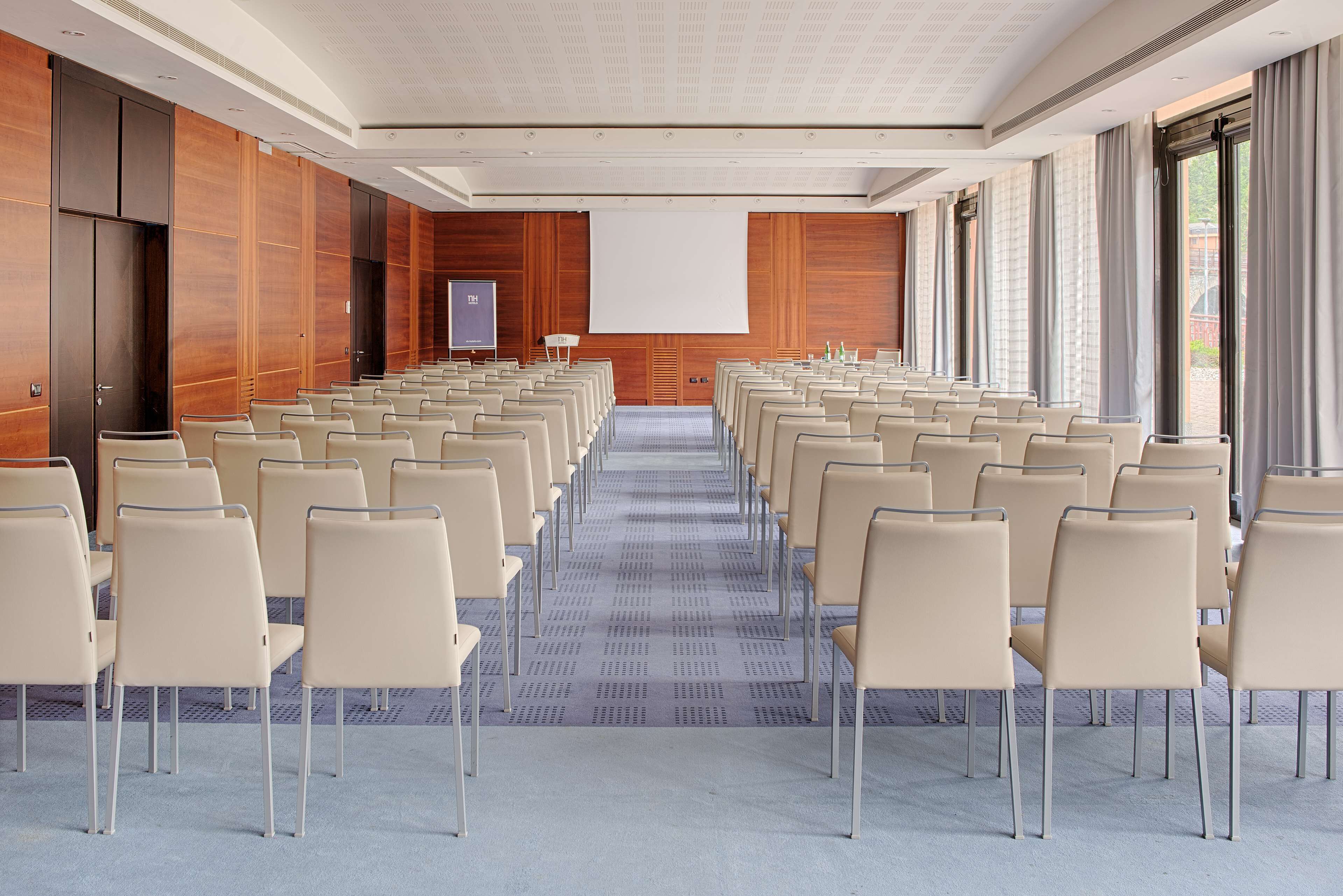 Una sala conferenze con file di sedie, uno schermo per proiettore e un'ampia finestra.